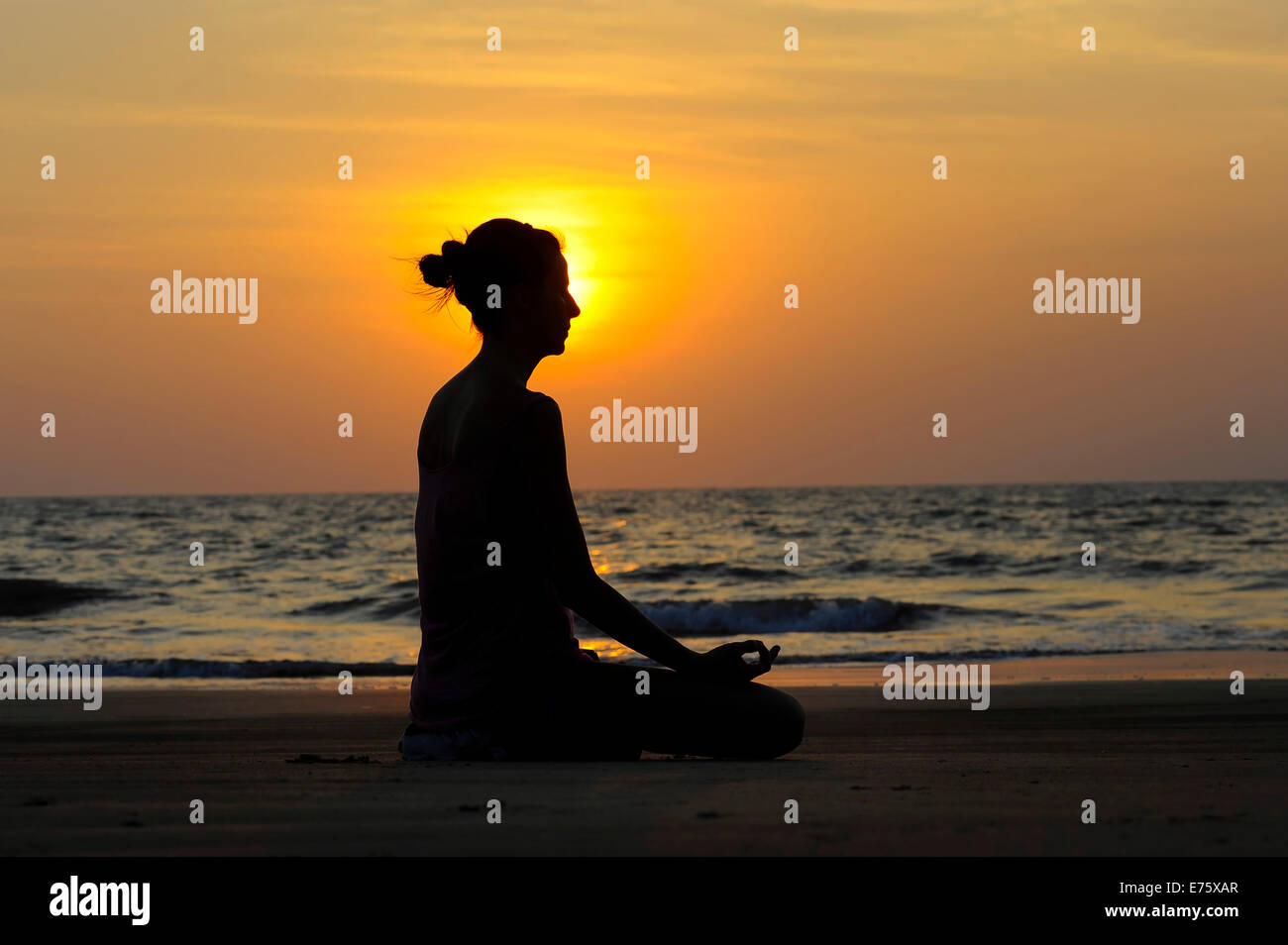 Femme méditant sur une plage au coucher du soleil, Kerala, Inde Banque D'Images