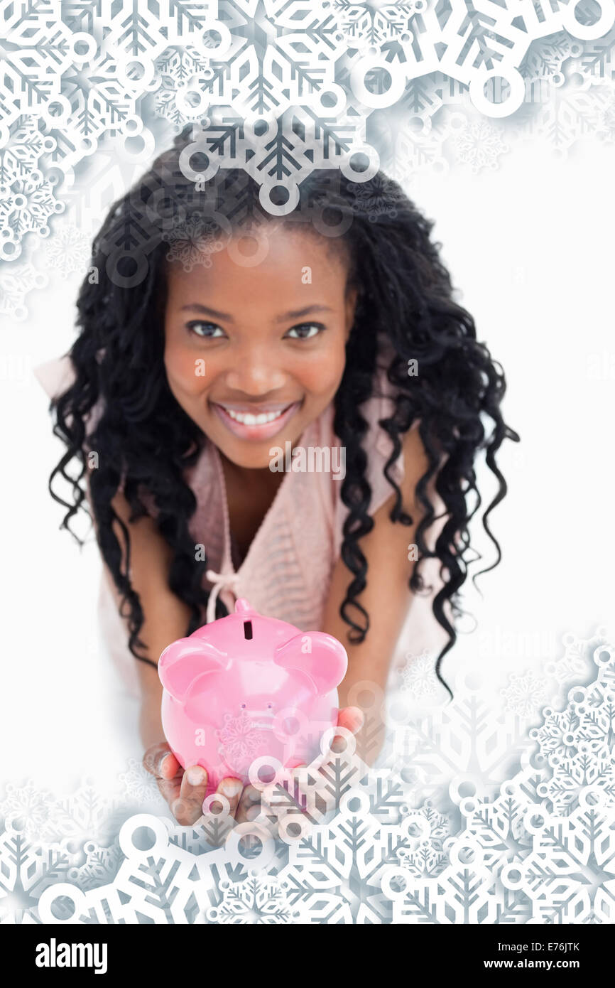 Composite image of a young woman smiling at the camera est holding a piggy bank dans ses mains Banque D'Images