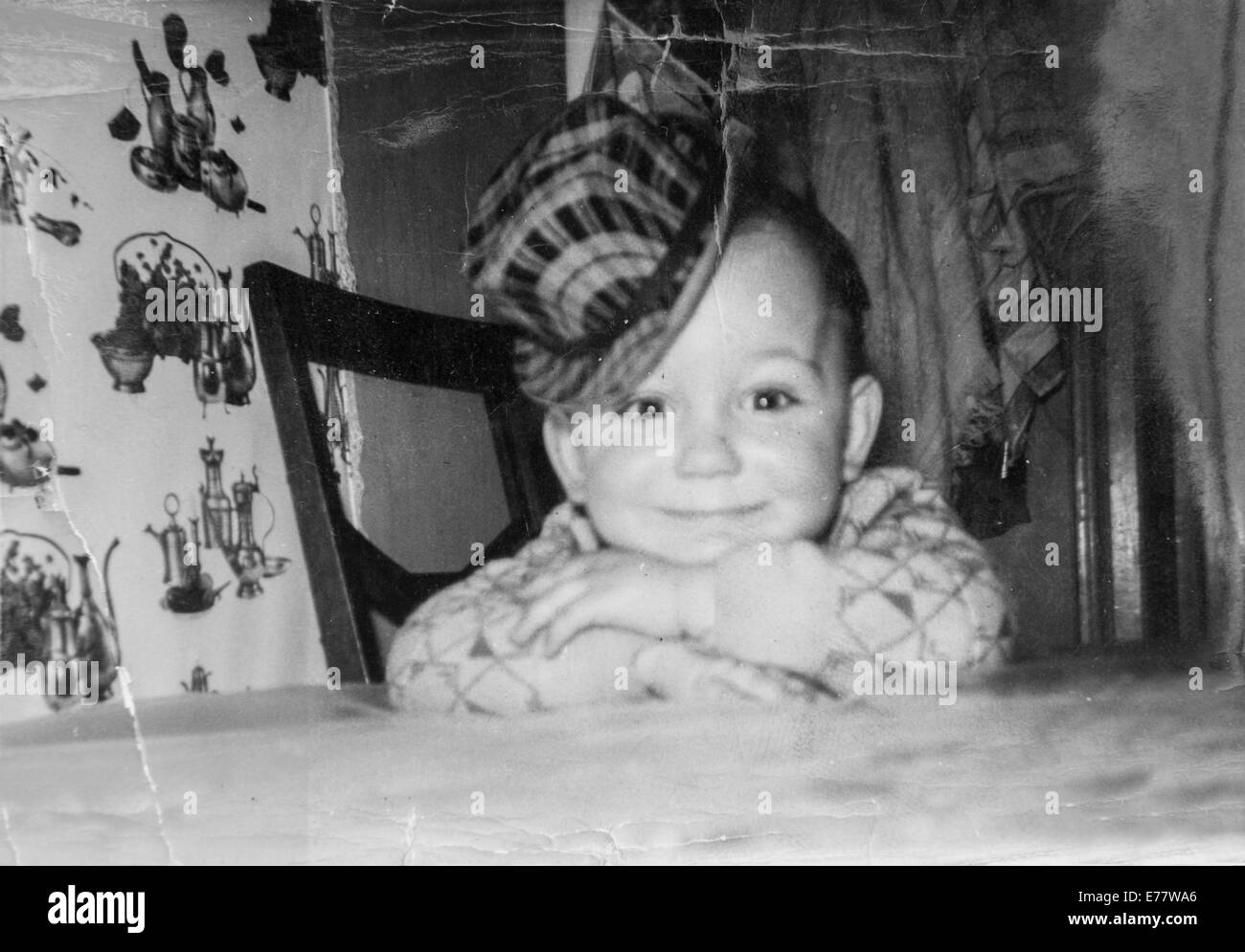 La photographie des années 60 montre un garçon avec un chapeau qui est assis à une table smiling Banque D'Images