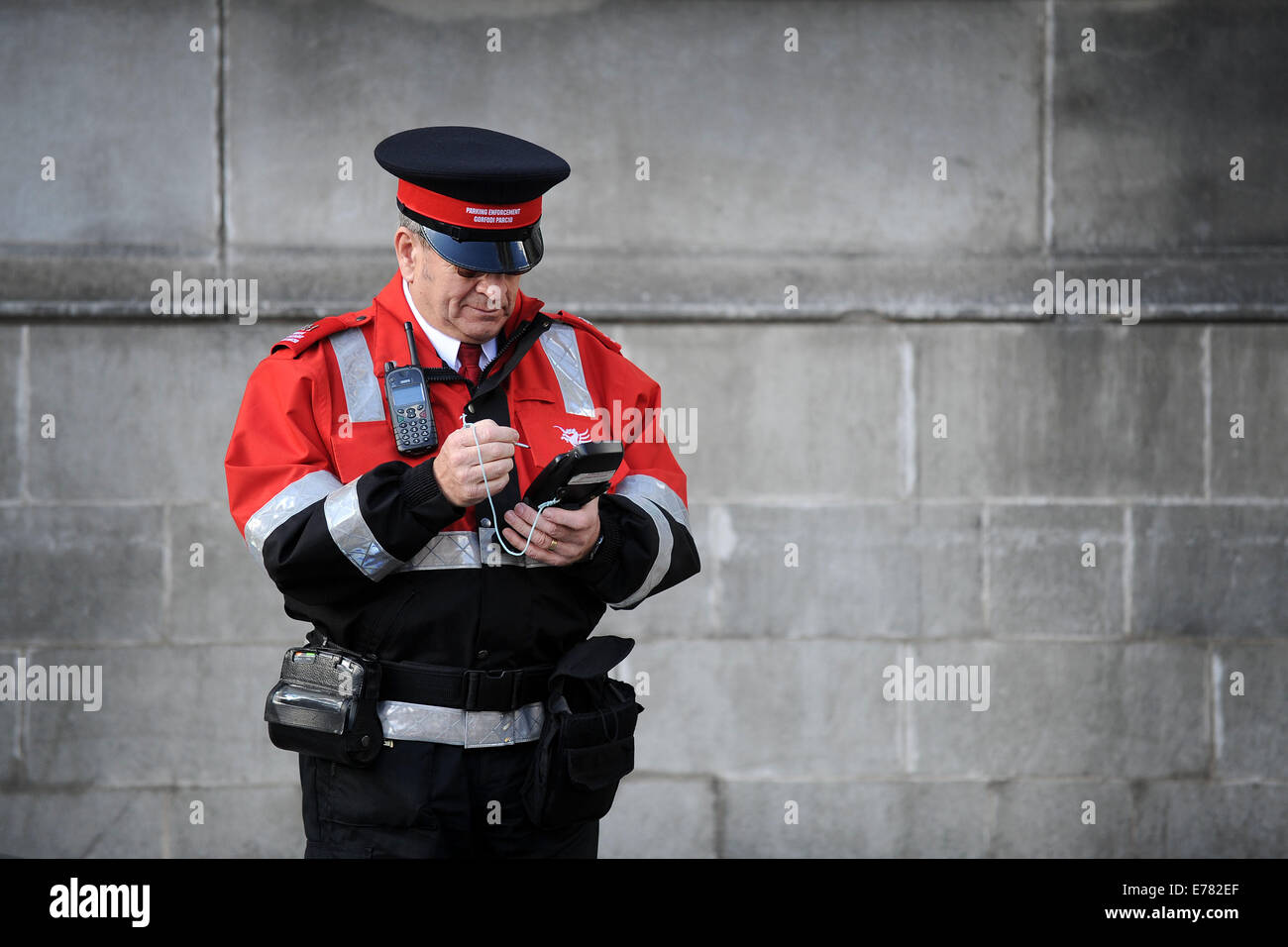 Un gardien de la circulation de billets de poche utilise une machine pour rendre une voiture en stationnement illégal à Cardiff au Pays de Galles. Banque D'Images