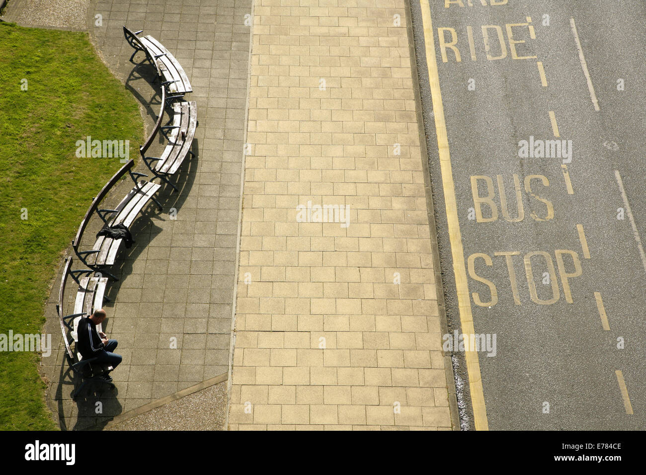 Homme assis sur le banc en bois courbé à un arrêt de bus. Banque D'Images