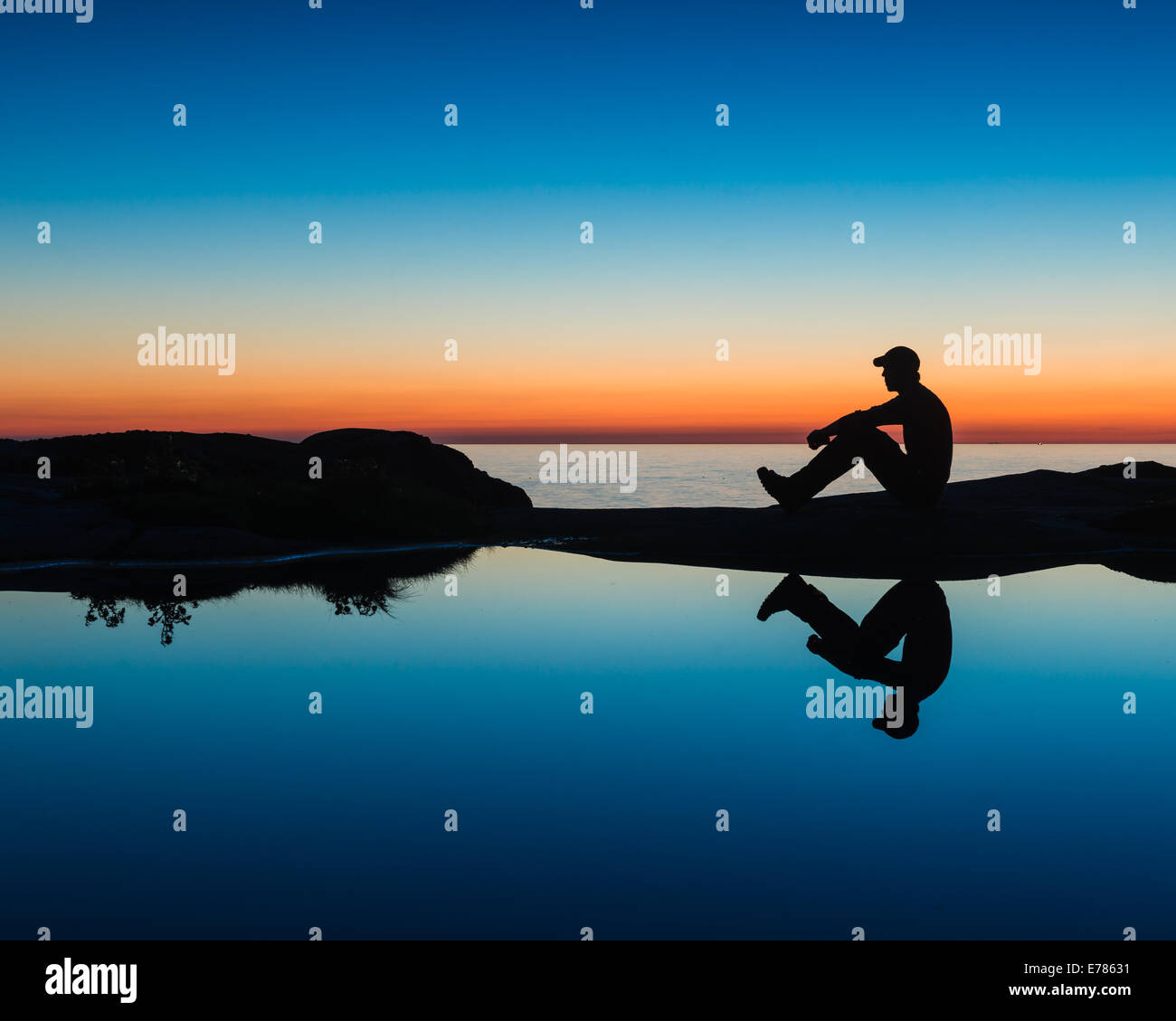 Silhouette d'un homme assis par une marée extérieure au coucher du soleil Banque D'Images