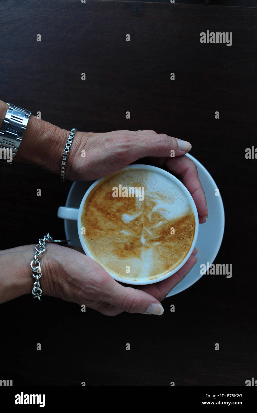 Mature Woman in cafe tenant une tasse de café cappuccino sur head voir Banque D'Images