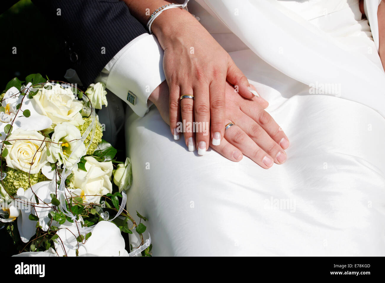 Les anneaux de mariage sur les mains, à côté du bouquet de mariée Banque D'Images