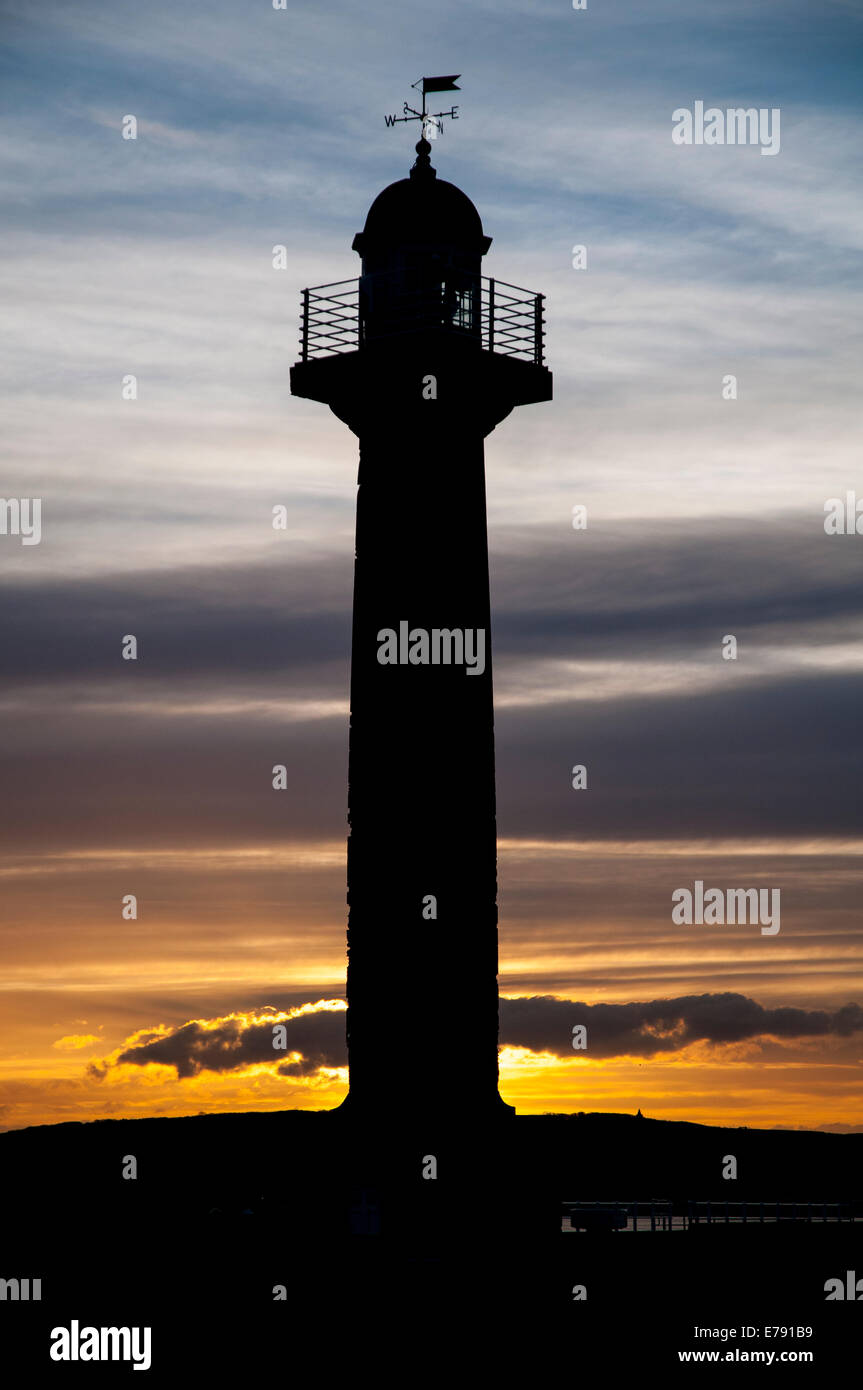 Le phare sur la jetée ouest silhouette sur le coucher du soleil à Whitby, North Yorkshire. Avril. Banque D'Images