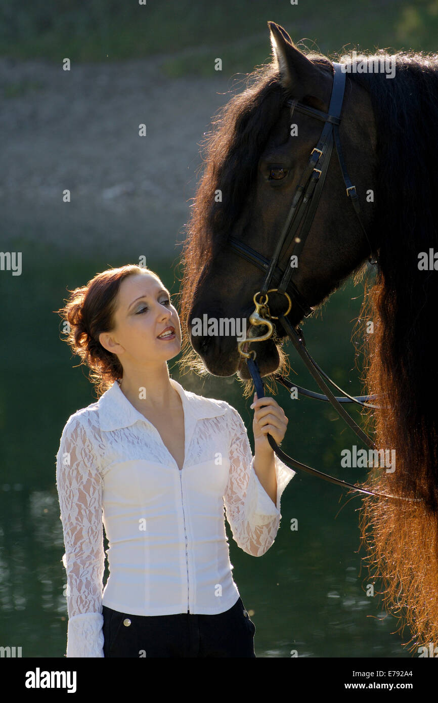 Jeune femme tenant un cheval frison noir au bord du lac, rétroéclairé, le nord du Tyrol, Autriche Banque D'Images