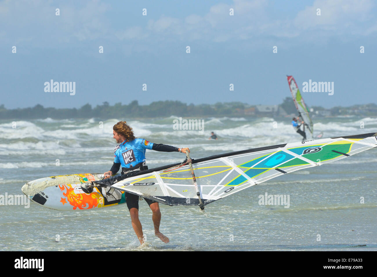 Man carrying windsurfer en mer agitée à West Wittering Beach, West Wittering, Chichester, West Sussex, Angleterre Banque D'Images