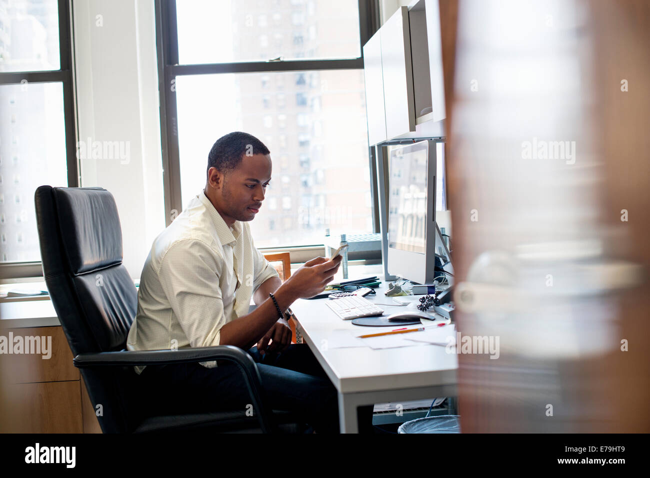 Un homme assis dans un bureau, contrôle son téléphone intelligent. Banque D'Images