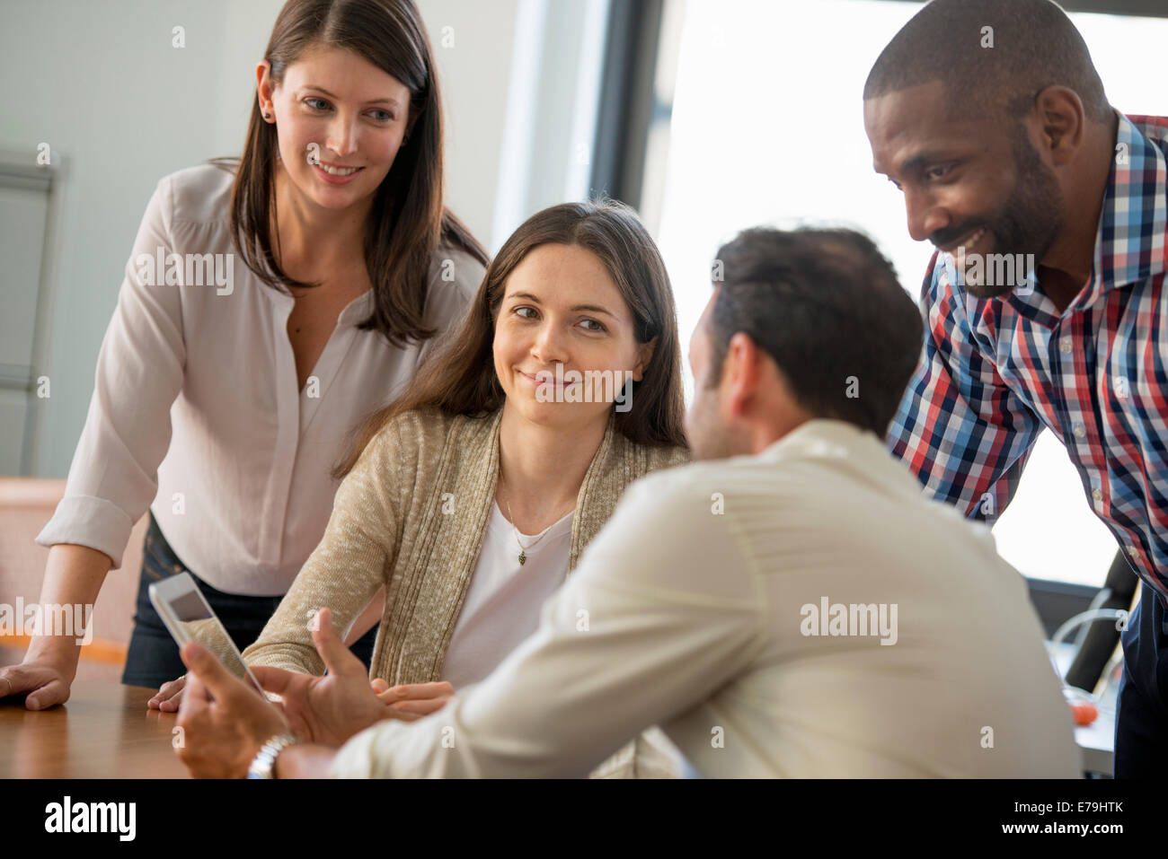 Quatre personnes, hommes et femmes, regroupés autour d'une tablette numérique, regarder l'écran. Banque D'Images