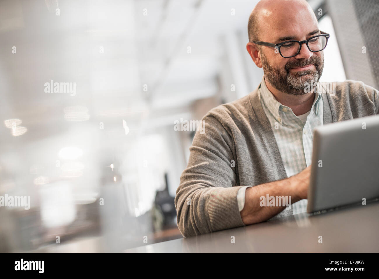 La vie de bureau. Un homme assis à une table, en train de travailler sur un ordinateur portable. Banque D'Images