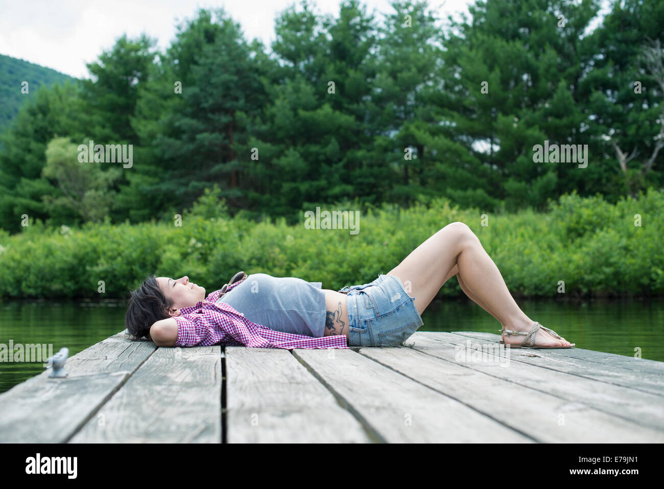 Une femme couchée sur la jetée par un lac en été Banque D'Images