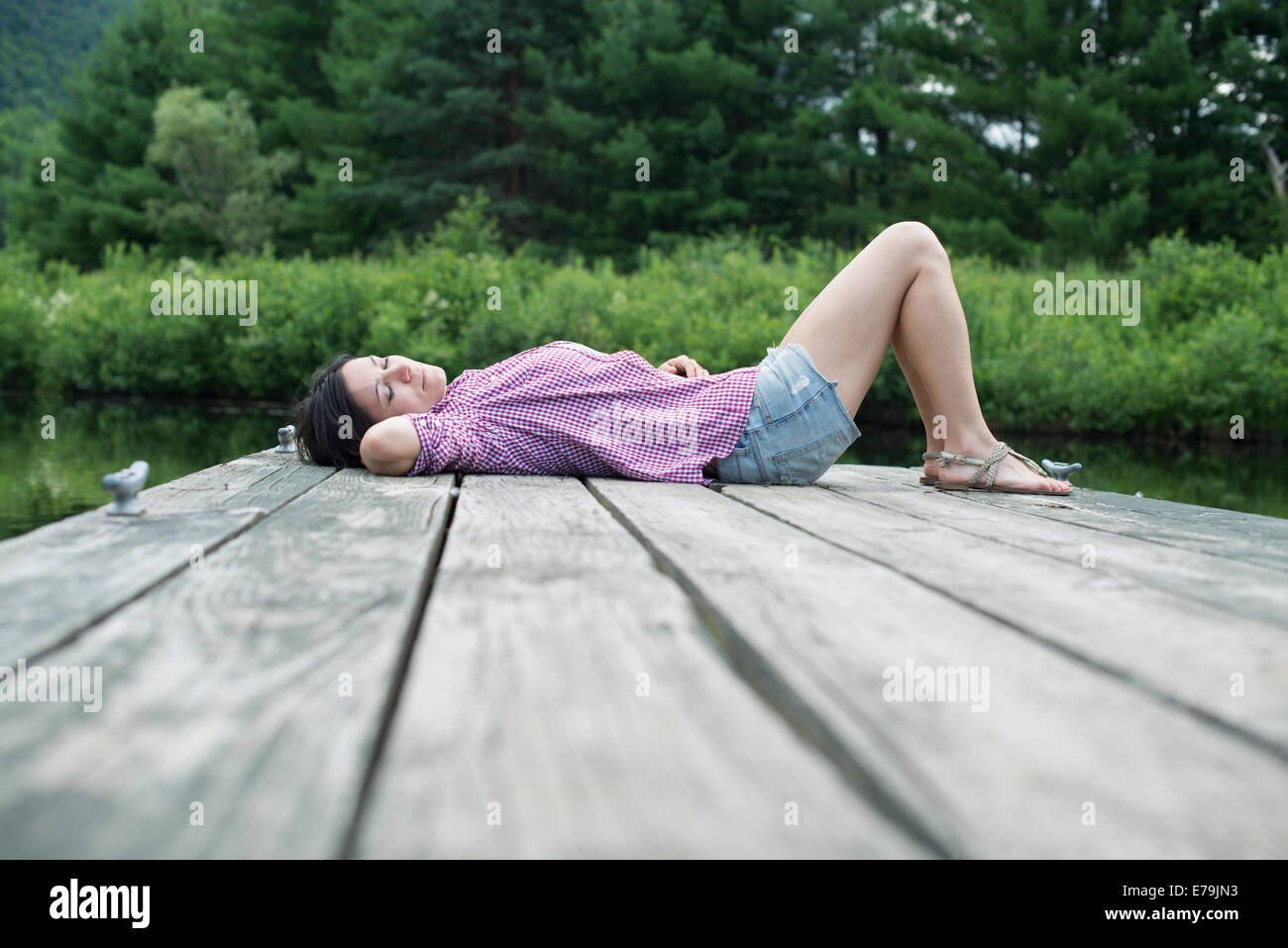 Une femme couchée sur la jetée par un lac en été Banque D'Images
