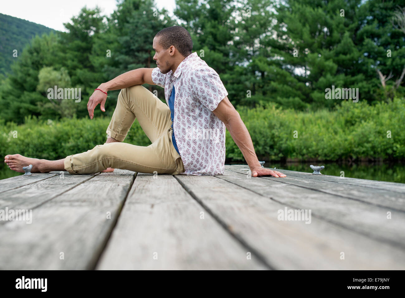 Un homme assis sur une jetée en bois d'un lac en été Banque D'Images