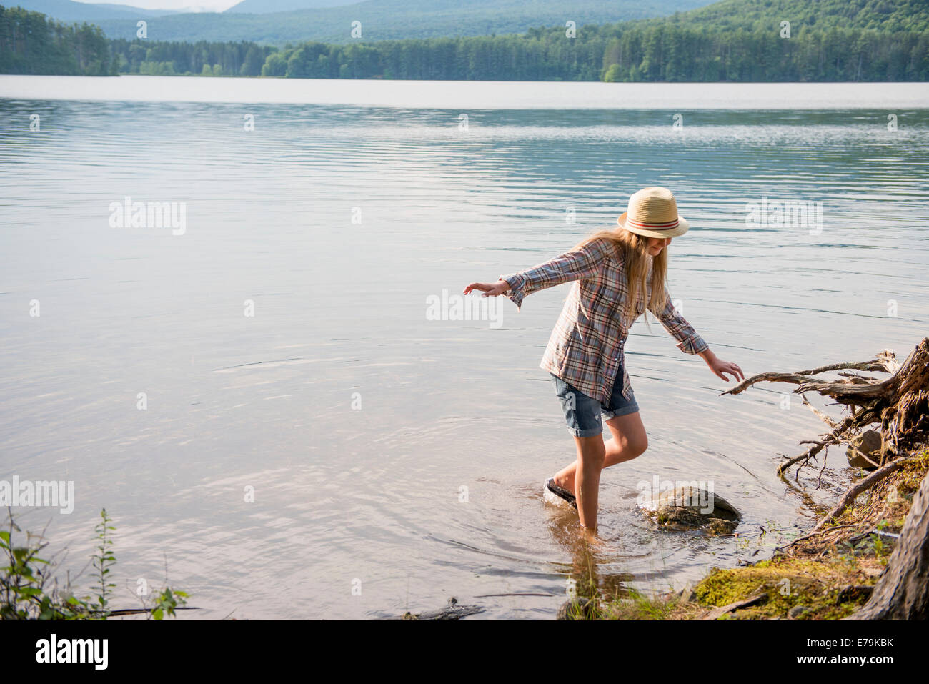 Une jeune fille dans un chapeau de paille et des courts-circuits pagayer dans les eaux peu profondes d'un lac. Banque D'Images