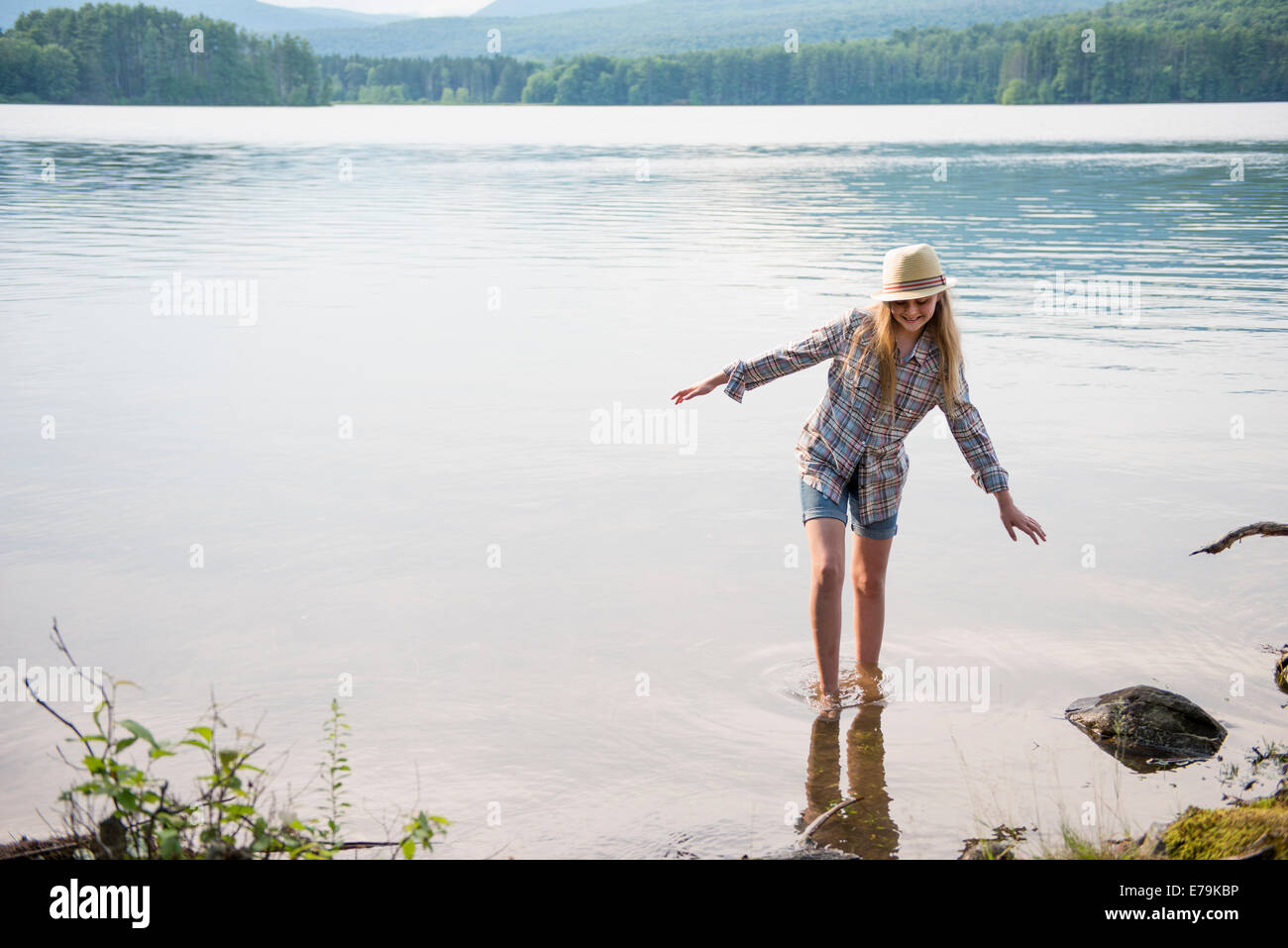 Une jeune fille dans un chapeau de paille et des courts-circuits pagayer dans les eaux peu profondes d'un lac. Banque D'Images