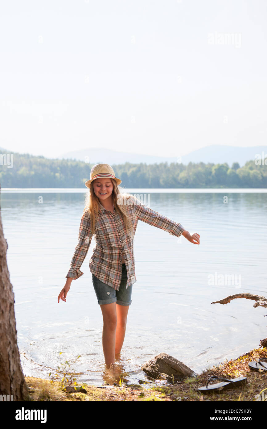 Une fille dans un chapeau de paille pagayer dans les eaux peu profondes d'un lac de montagne. Banque D'Images
