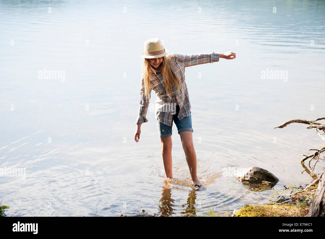 Une fille dans un chapeau de paille pagayer dans les eaux peu profondes d'un lac de montagne. Banque D'Images