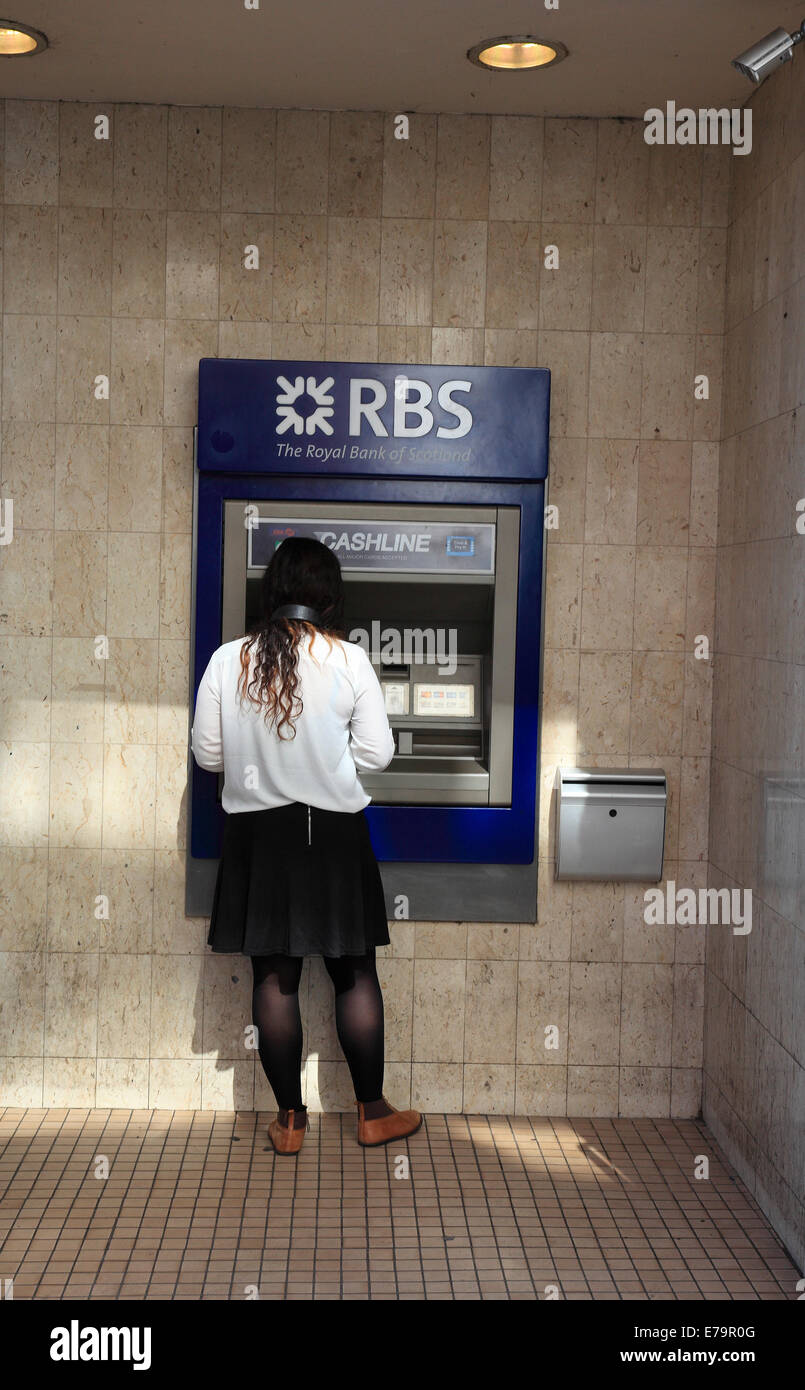 Une jeune femme se retire de l'argent d'un distributeur automatique de RBS. Banque D'Images