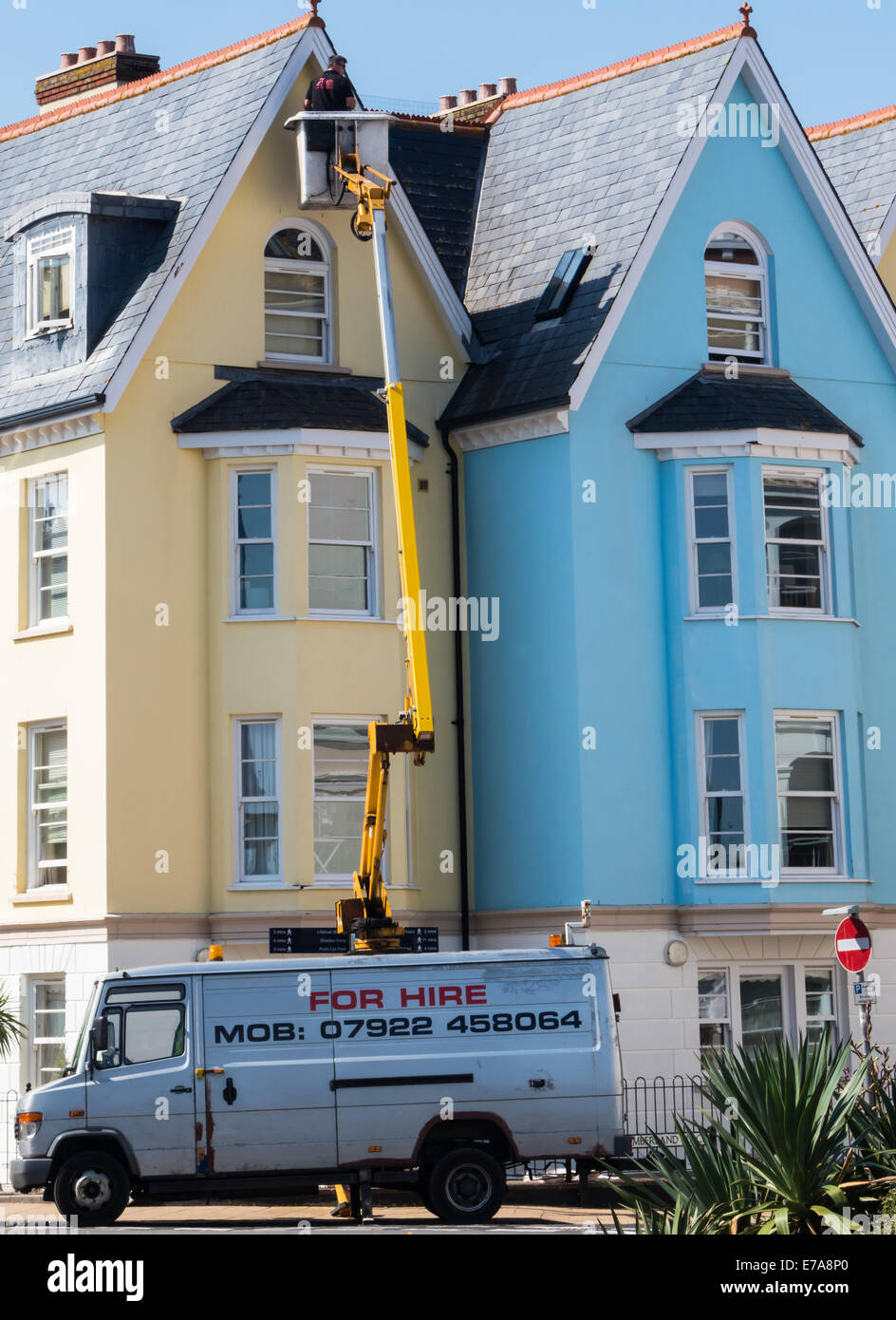 Teignmouth, Devon, Angleterre. Un homme sur une grue peinture 4 histoires sur le côté d'un bâtiment. Banque D'Images