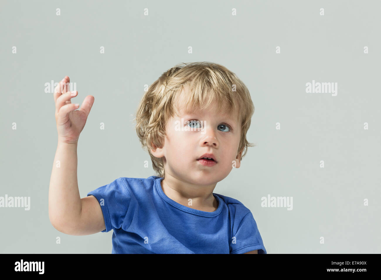 Cute baby boy looking up avec la main posée sur fond gris Banque D'Images