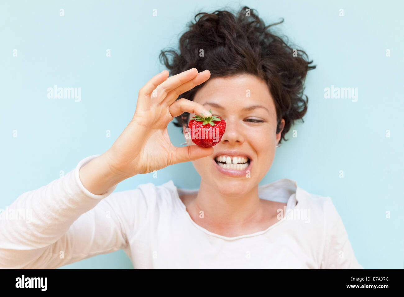 Une femme se serrant les dents tout en maintenant la fraise sur fond bleu Banque D'Images