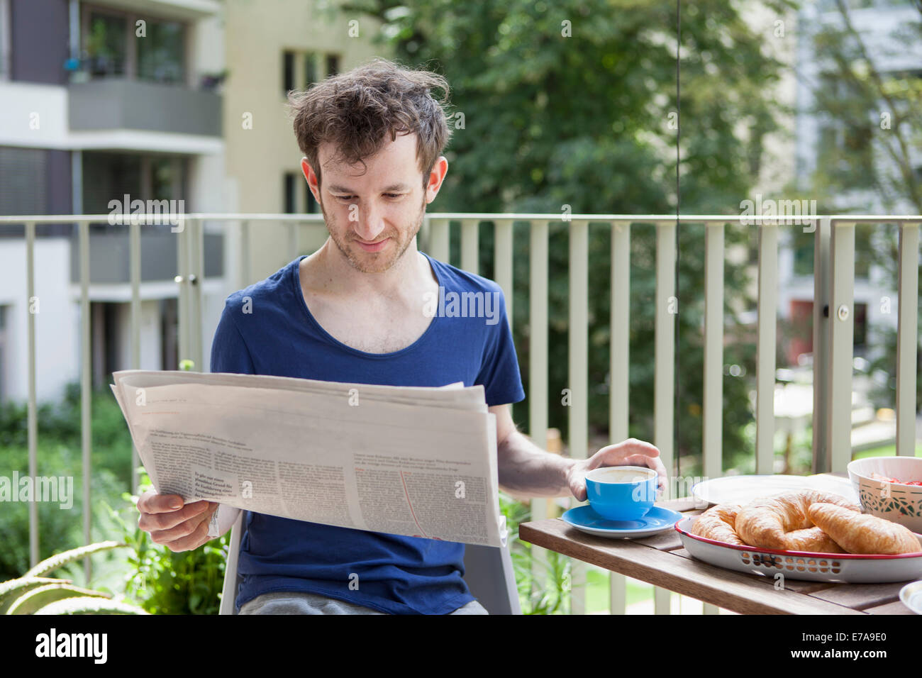 Jeune homme lisant le journal pendant le petit-déjeuner à portique Banque D'Images