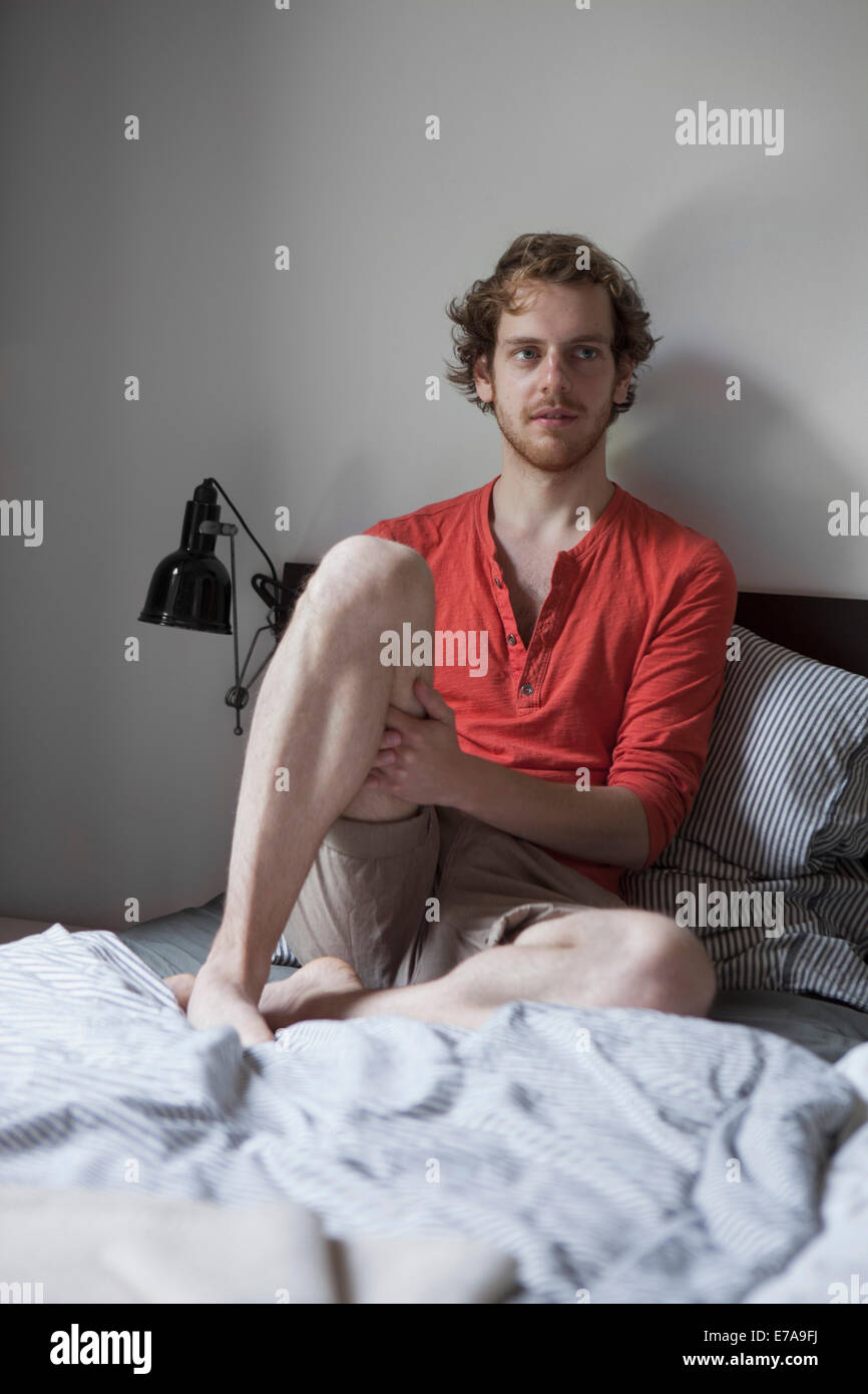 Young man sitting on bed at home Banque D'Images