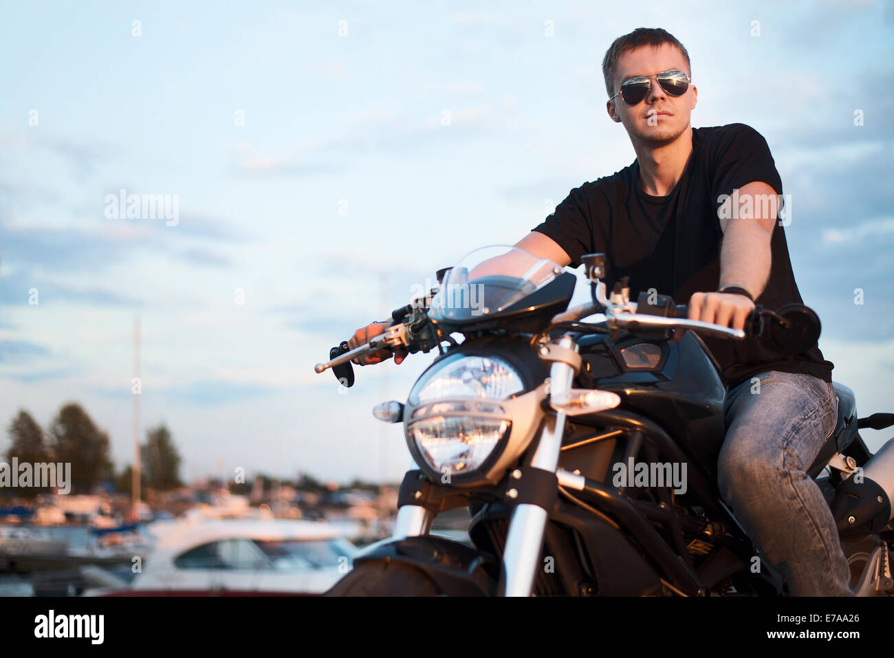 Beau portrait romantique biker Homme à lunettes se trouve sur un vélo sur un coucher du soleil près du lac et du club de yacht de gauche de l'espace de copie. Banque D'Images