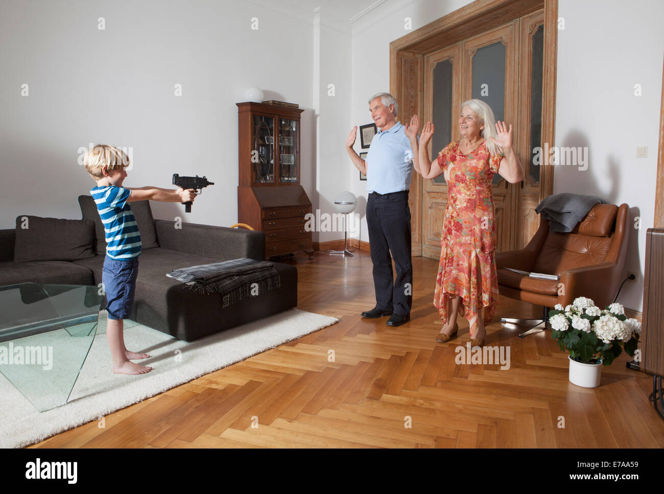 Petit garçon visant avec pistolet jouet vers les grands-parents à la maison Banque D'Images