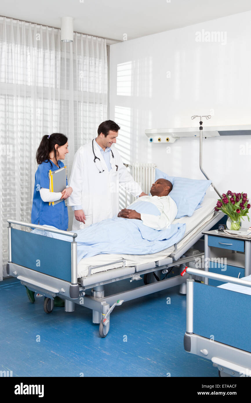 Un médecin et l'infirmière parler à un patient allongé sur un lit d'hôpital Banque D'Images