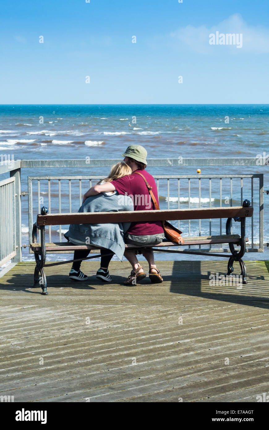 Un jeune couple assis sur edge Teignmouth Pier en voyant la mer. Banque D'Images