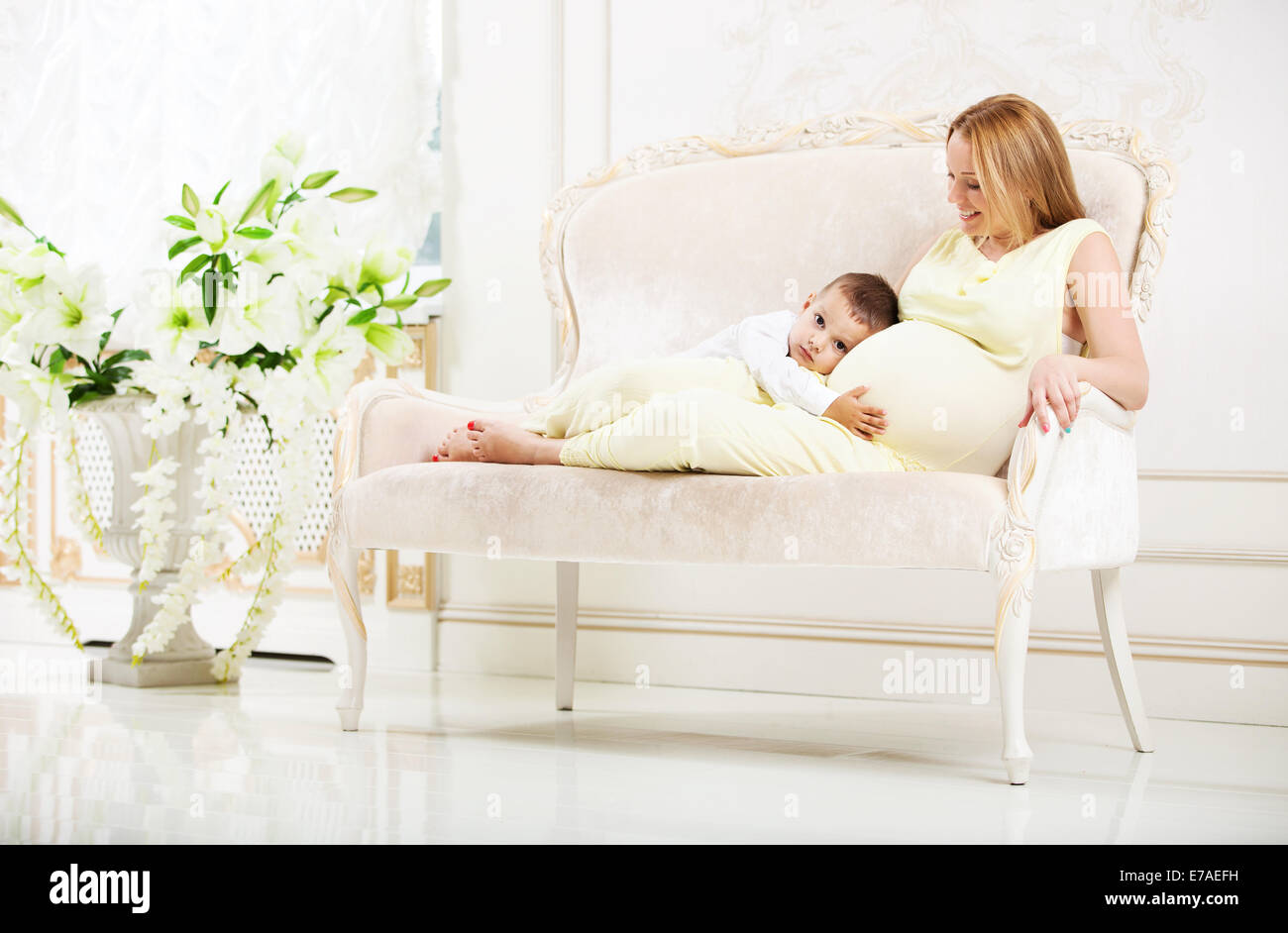 Petit garçon à l'écoute de son ventre femme enceinte en position couchée sur la table à la maison Banque D'Images