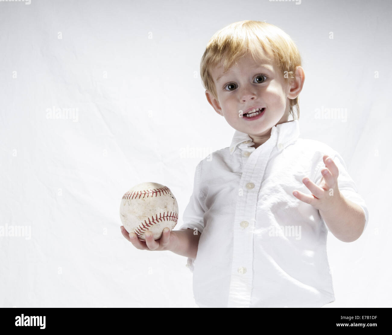 Jeune garçon dans une chemise blanche tenant une balle molle. Le fond est blanc, il a des cheveux blonds. Clermont Floride USA Banque D'Images