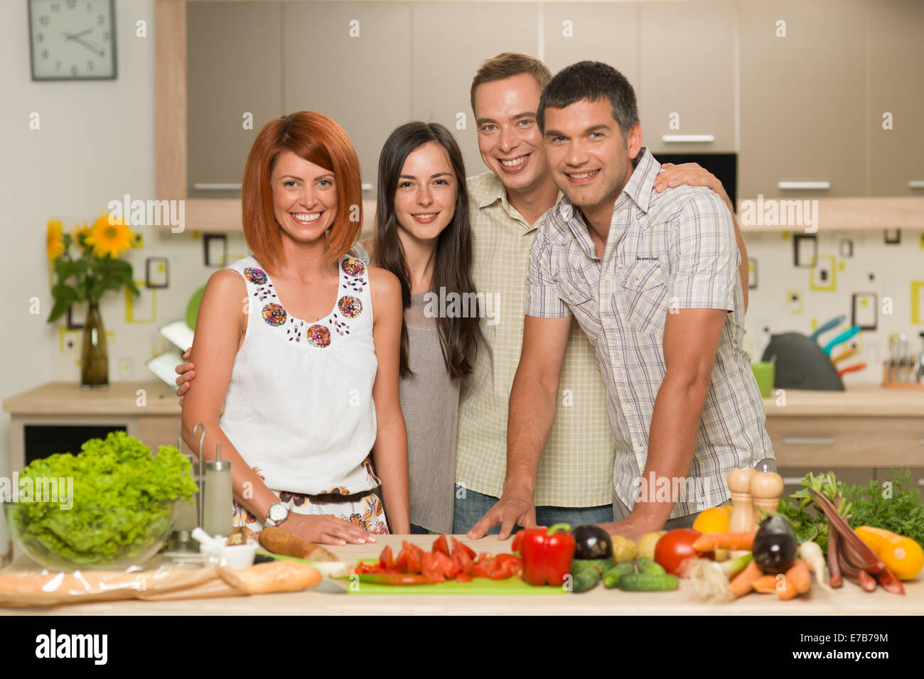 Vue avant du young caucasian friends standing dans la cuisine et souriant, avec des légumes sur la table Banque D'Images