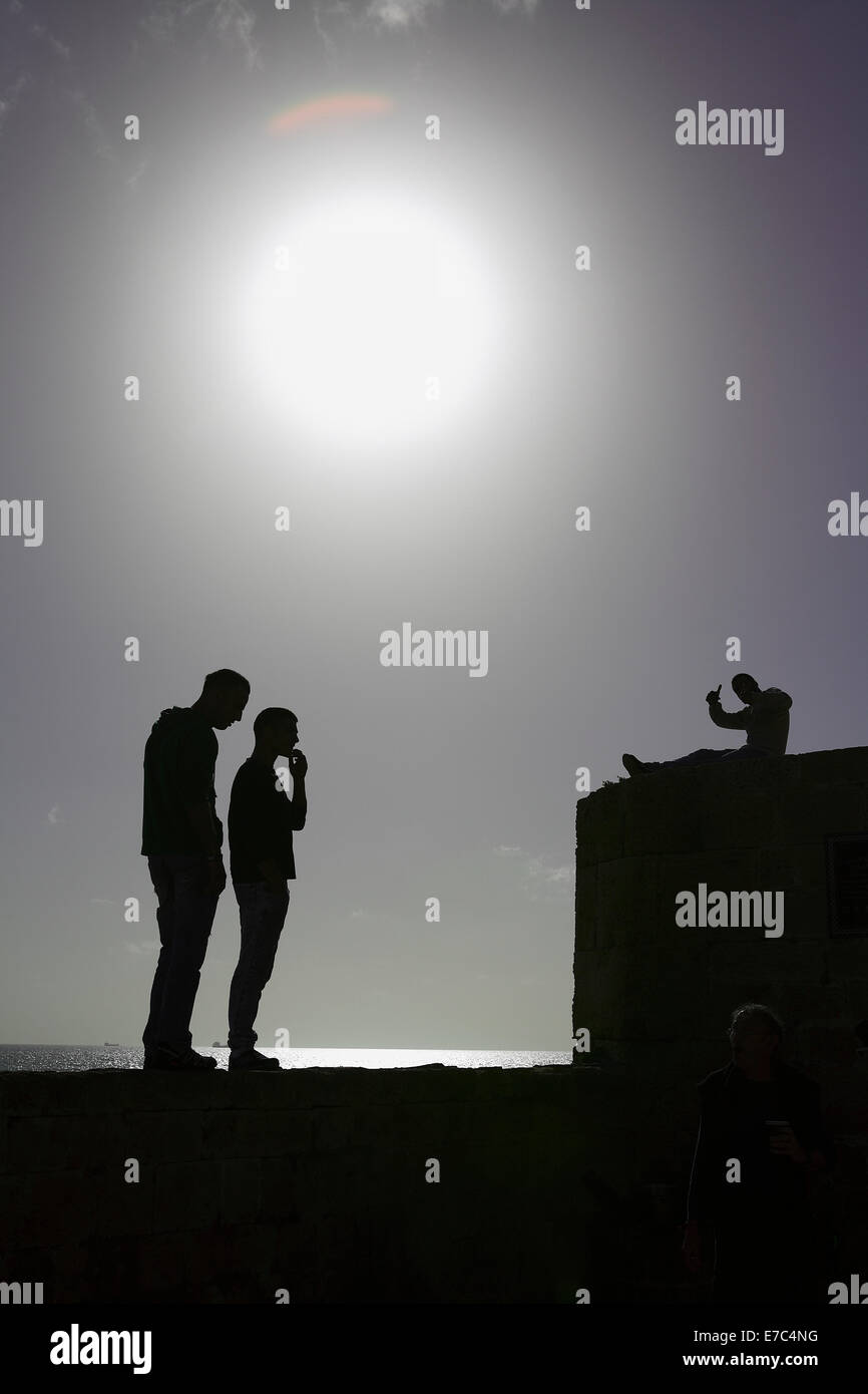 Trois personnes assises sur le mur en rétroéclairage brillant dans la vieille ville d'acre au nord d'israël Banque D'Images