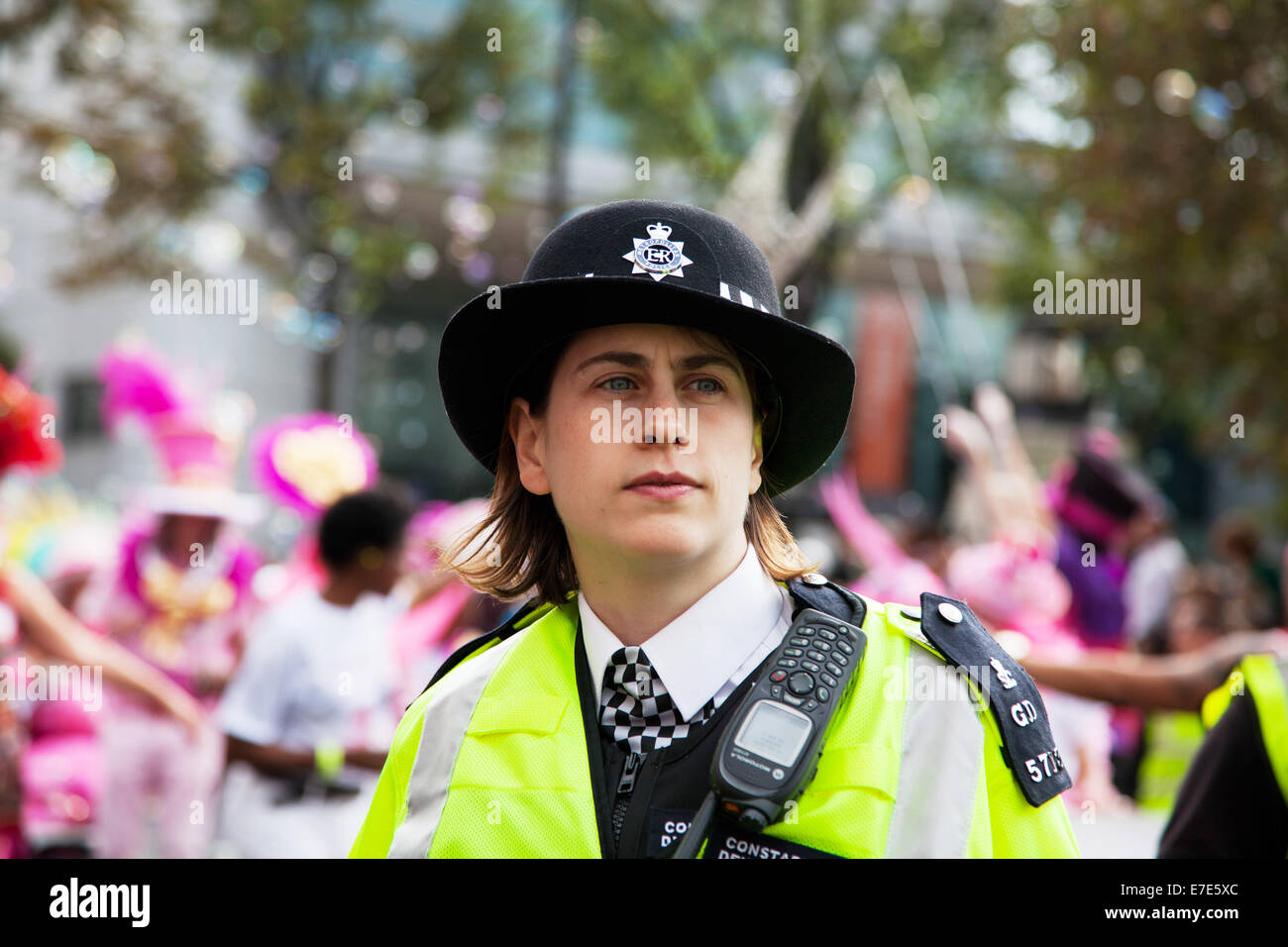 Une jeune femme policier garde un œil sur la foule heureuse et la spectaculaire procession à l'extérieur de ville de Hackney. Banque D'Images