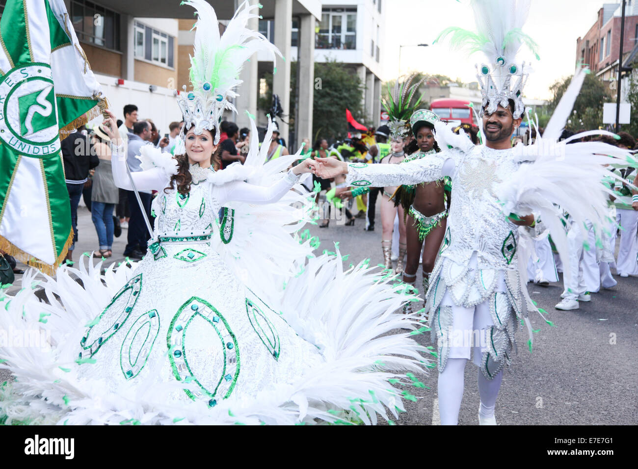 Un couple habillé en vert et blanc laisse une partie de la procession se tenant la main et un drapeau. Banque D'Images