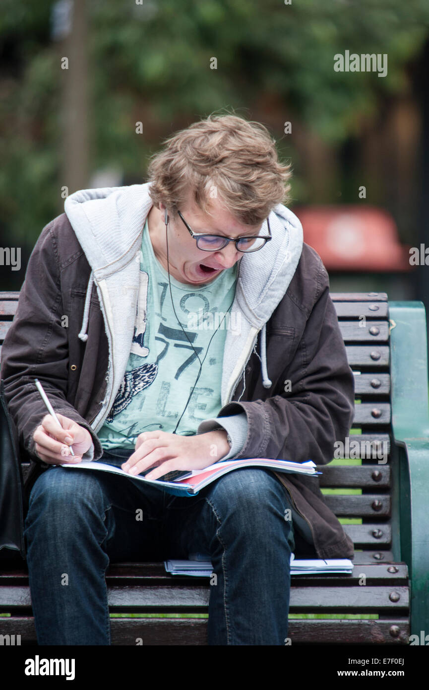 Étudiant masculin bâillant étudiant sur un banc à l'extérieur de la bibliothèque de l'État de Melbourne, Australie, montrant la fatigue et le stress des examens pendant les études universitaires. Banque D'Images