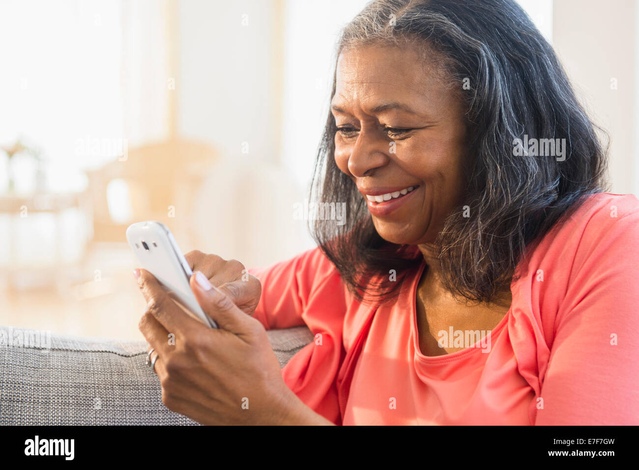 Mixed Race woman using cell phone on sofa Banque D'Images