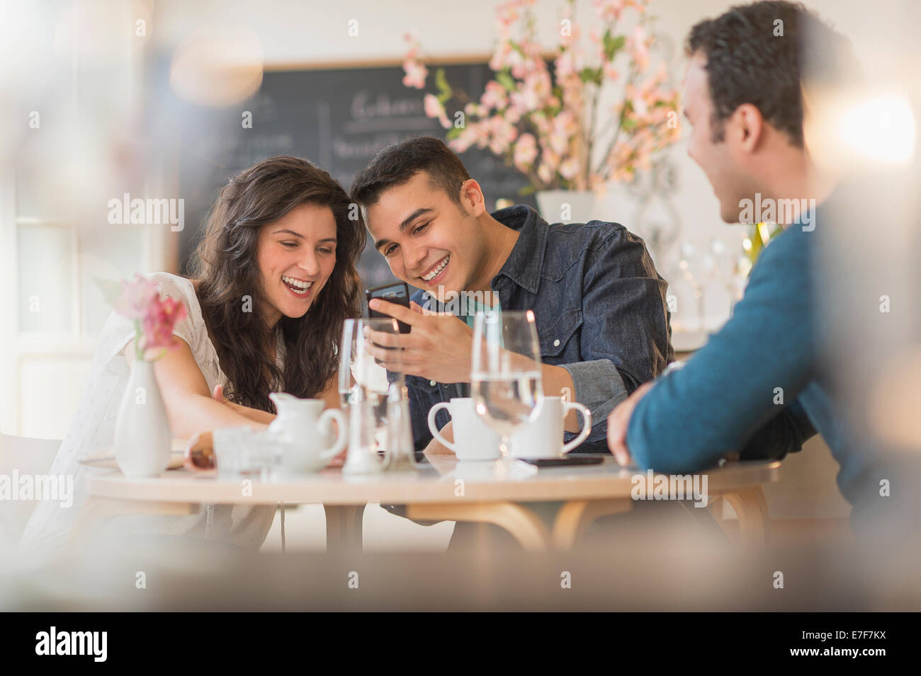 Amis hispaniques using cell phone in cafe Banque D'Images