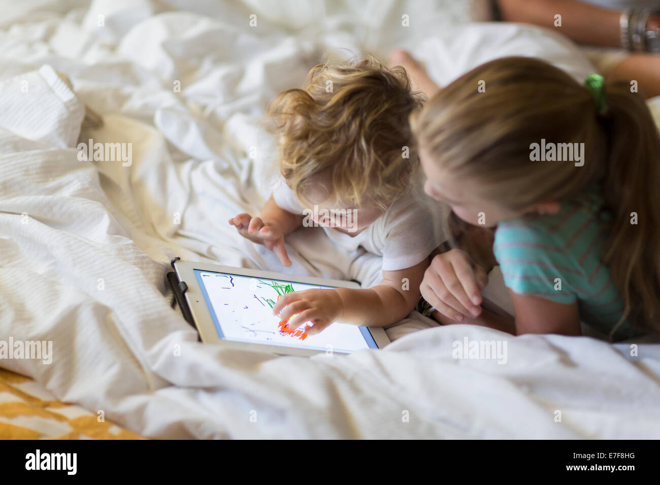 Caucasian girl et tout-petit frère using tablet computer on bed Banque D'Images