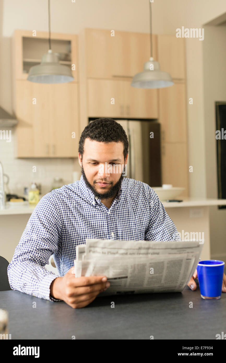 Mixed Race man reading newspaper at breakfast table Banque D'Images