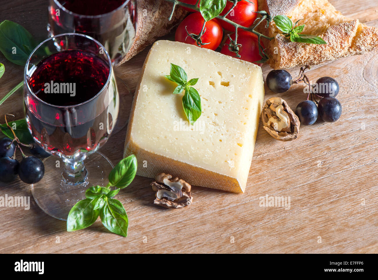 Vin rouge avec le fromage, les noix, les tomates, les feuilles de basilic et les raisins. ingrédients alimentaires à faible clés photo style. Banque D'Images