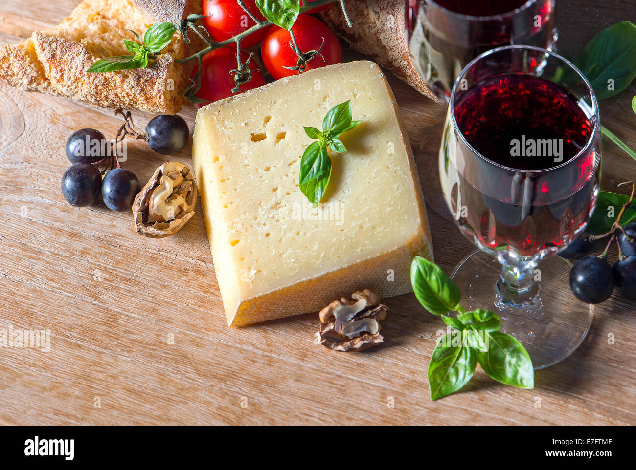 Vin rouge avec le fromage, les noix, les tomates, les feuilles de basilic et les raisins. ingrédients alimentaires à faible clés photo style. Banque D'Images