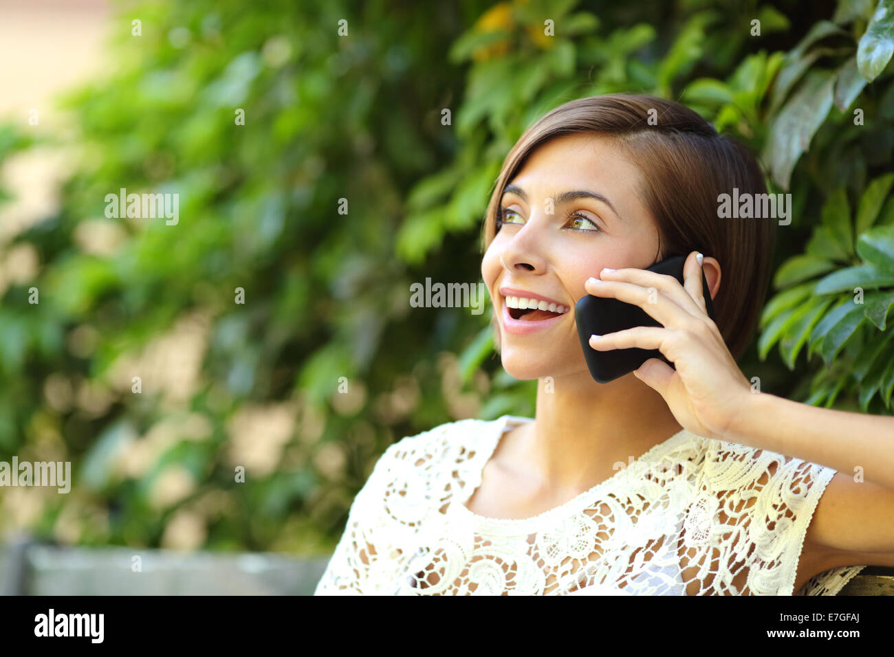 Casual femme heureuse au téléphone dans un parc assis sur un banc avec un arrière-plan flou vert Banque D'Images