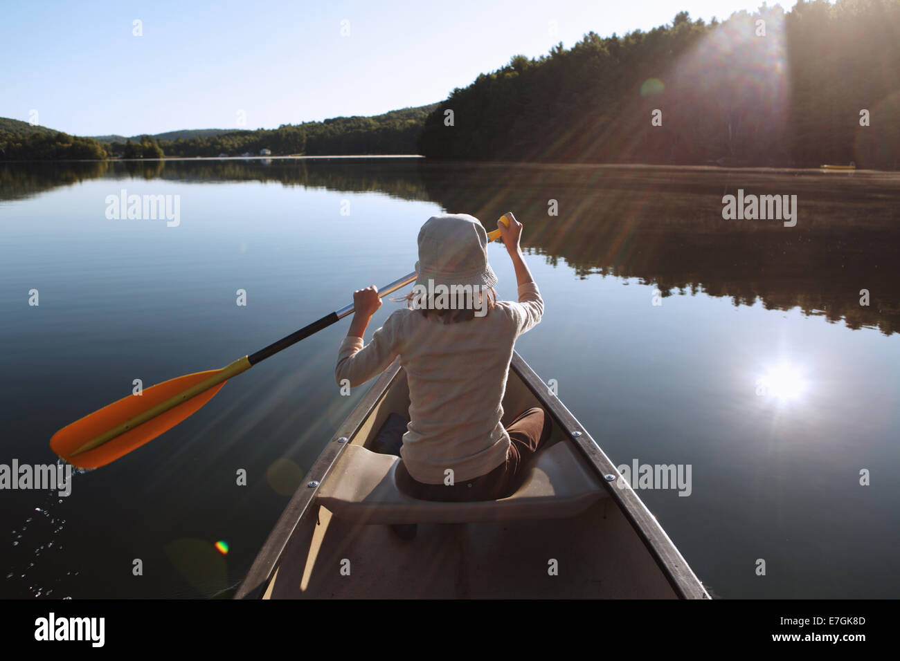 Jeune fille de canots sur un lac calme au lever du soleil Banque D'Images