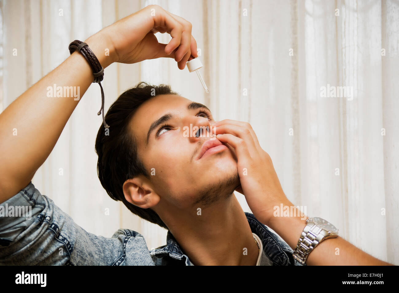 Beau jeune homme dropping medicine dans son oeil avec compte-gouttes Banque D'Images