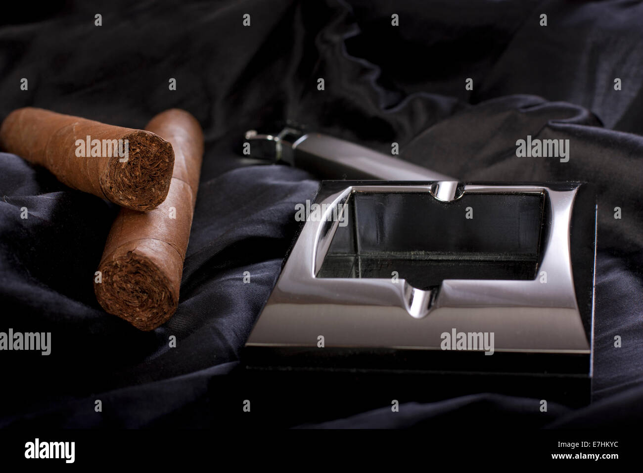 Close up of metallic cendrier, briquet et cigare cubain sur fond de soie noire Banque D'Images