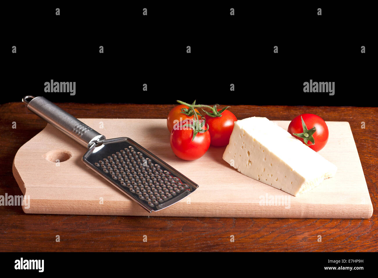 Râpe à fromage, tomate rouge et sur un bureau en bois Banque D'Images