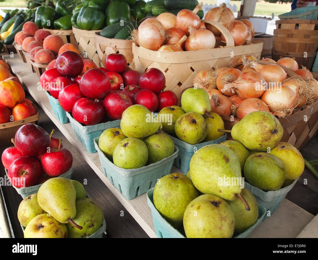 Paniers de poires fraîchement récoltées en vert, pommes rouges, oignons jaunes d'or et d'autres sont en vente à un stand en bordure de la produire. Banque D'Images